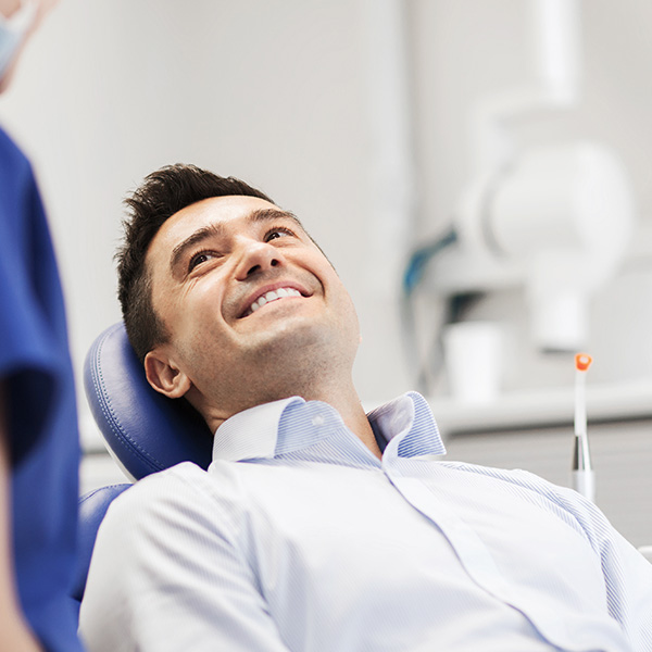 The image shows a man sitting in a dental chair, smiling and looking at the camera.