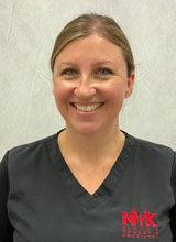 A smiling woman in a white lab coat, standing against a plain background.