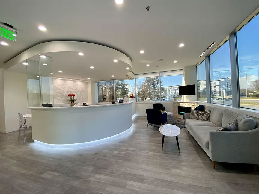 The image displays a modern, well-lit office space with a reception area featuring a curved counter and a waiting area furnished with contemporary seating.