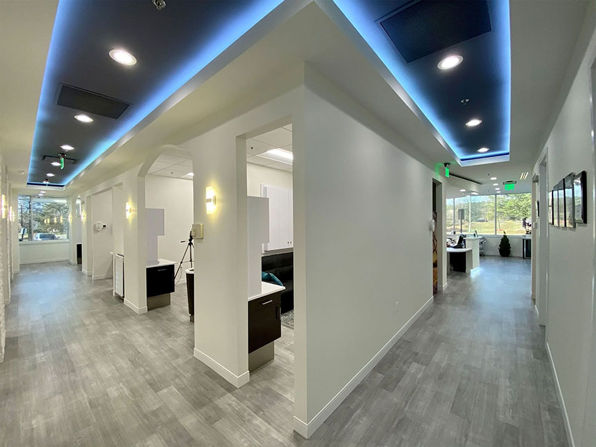 The image shows an interior space that appears to be a waiting area or reception room, with a modern design featuring white walls, grey flooring, and contemporary furnishings.