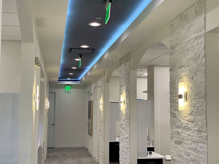The image depicts an interior hallway of a building with a series of light fixtures, white walls, and a modern design.