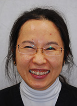 A smiling woman with glasses, wearing a white blouse and a dark cardigan, against a neutral background.