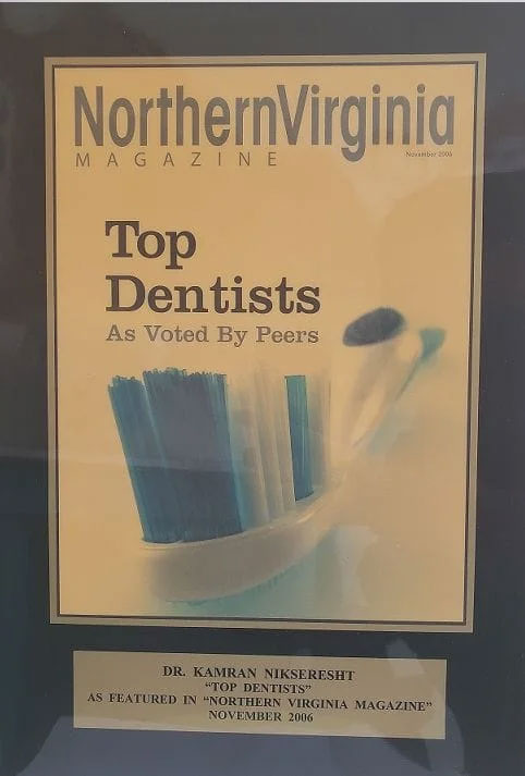 An image of a framed award or recognition with text that reads 'NORTHERN VIRGINIA MAGAZINE TOP DENTISTS AS VOTED BY PEERS,' featuring a photograph of a toothbrush with blue bristles.