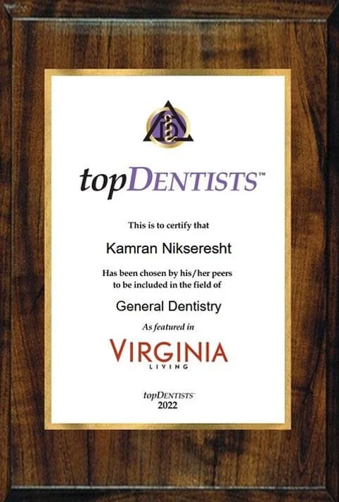 The image displays a framed certificate on a wooden surface, featuring text and logos. It is an award or recognition from  Top Dentists  for a dental professional named Kaman Nisheth, who holds the title of General Dentistry at Virginia Living Magazine.