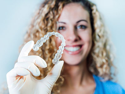 A woman holding a transparent bracelet with dental-like structures in her hand, set against a white background.