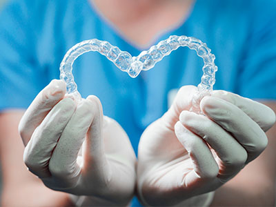 A person s hands holding a heart-shaped object that looks like a clear, transparent dental retainer with a blue background.