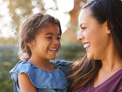 A woman and a young child are smiling at the camera, with both of them looking towards each other.