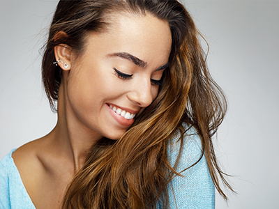 A woman with long brown hair, wearing a light blue top, smiling gently at the camera.