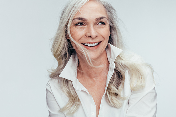 A woman with short hair, wearing a white top and smiling broadly at the camera.