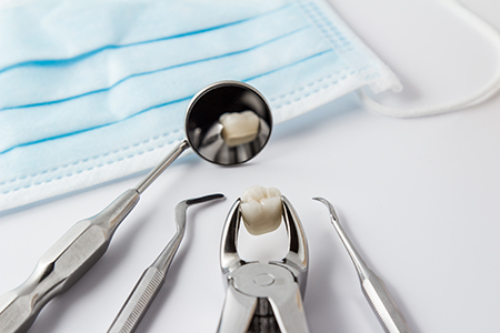 A collection of dental instruments on a table, with a blue surgical mask and a small tray of dental tools in the foreground.