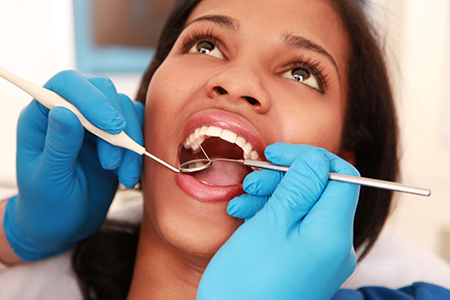 A woman in a dental chair receiving oral care, with a dental professional performing an examination or procedure.