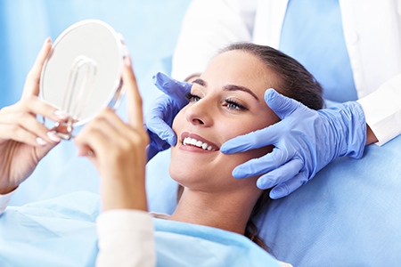 A woman in a medical setting is receiving dental care, with a dentist using a magnifying glass to examine her teeth.