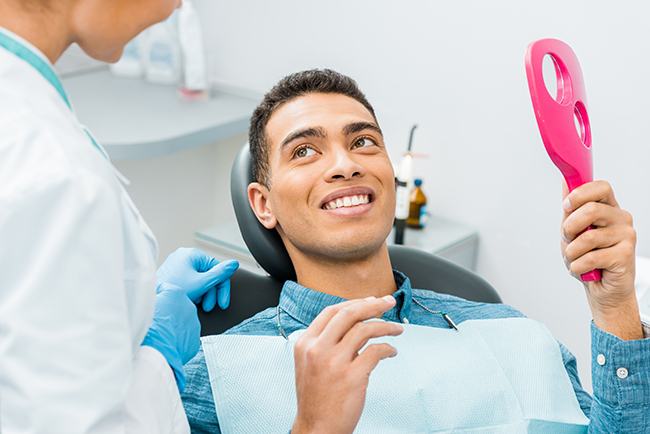 A man in a dental chair, smiling at the camera, with a dental hygienist standing beside him.