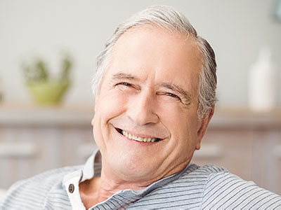 The image shows an elderly man with a smile, sitting in a relaxed posture.