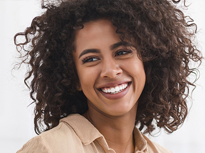 A smiling woman with curly hair, wearing a brown top and earrings.